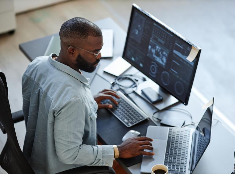 Minimal high angle view at African American software developer working with computers and data systems in office