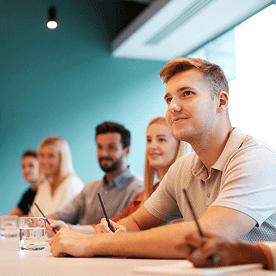 Man in beige shirt holding pen at meeting table with colleagues in modern office with teal walls