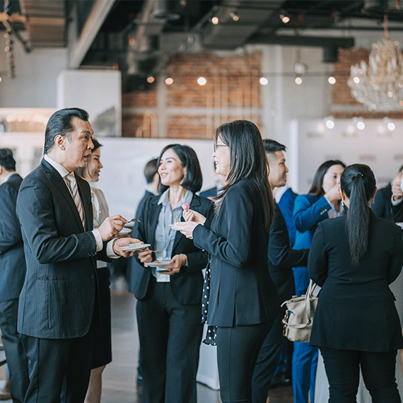 Business professionals networking at an indoor event with exposed brick walls and modern lighting in the background.
