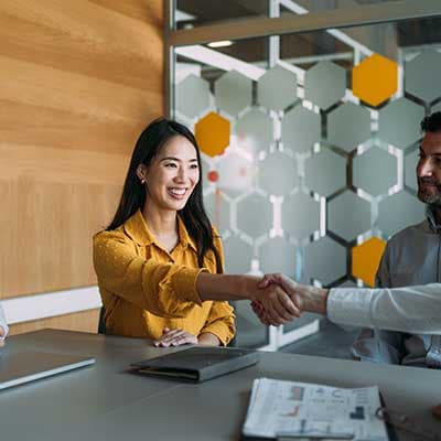 Two professionals shaking hands in modern office with hexagonal wall panels and wooden accents.