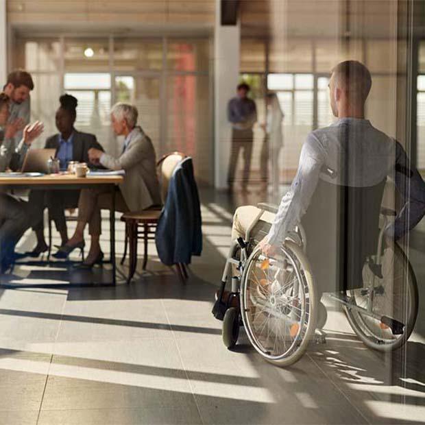 Rear view of a businessman in a wheelchair arriving on a meeting with his colleagues in the office. The view is through glass.