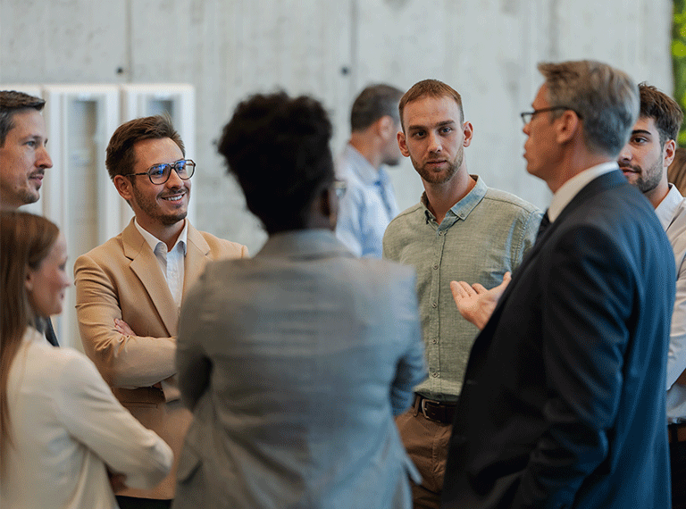 Business professionals in business casual and formal attire engaged in conversation during an office meeting or networking event.